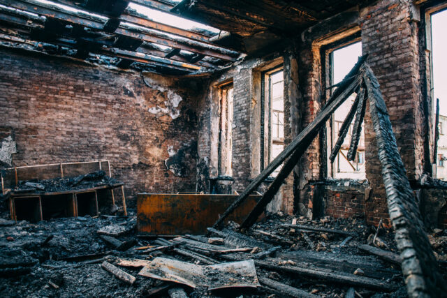 Burnt room interior with walls, furniture and floor in ash and coal, ruined building after fire, toned